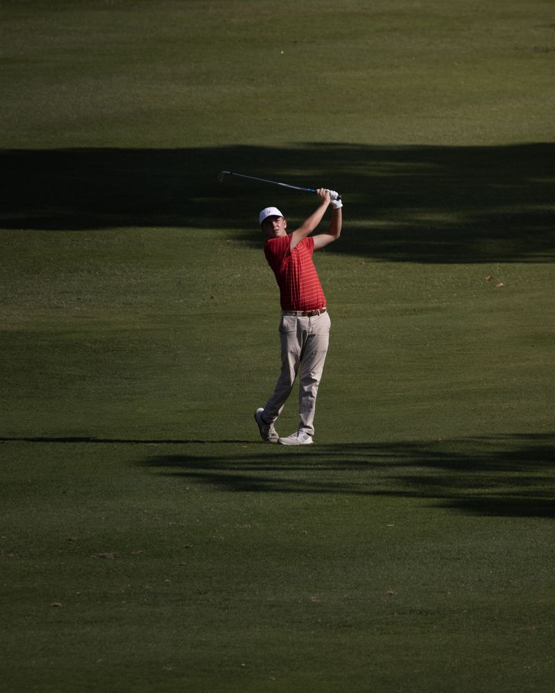 A golfer in red follows through on a fairway in late light