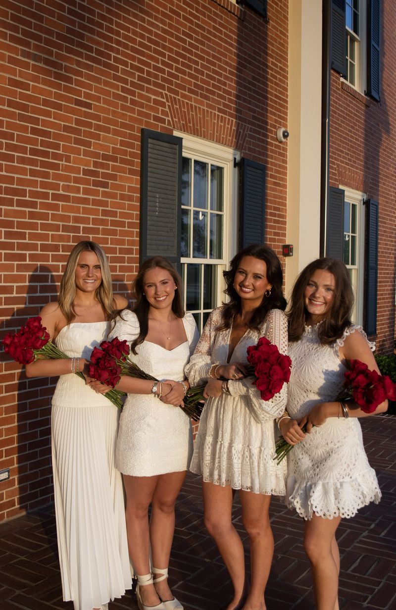 Four young women in white dresses with red roses