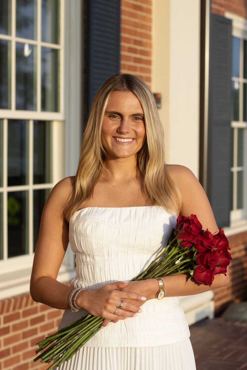 A young woman in a white dress holds red roses