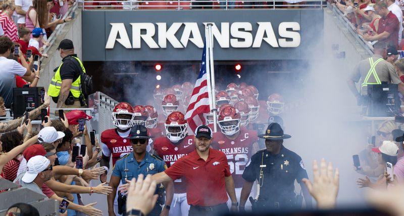 Razorback football players run out of the Arkansas tunnel through smoke with an American flag