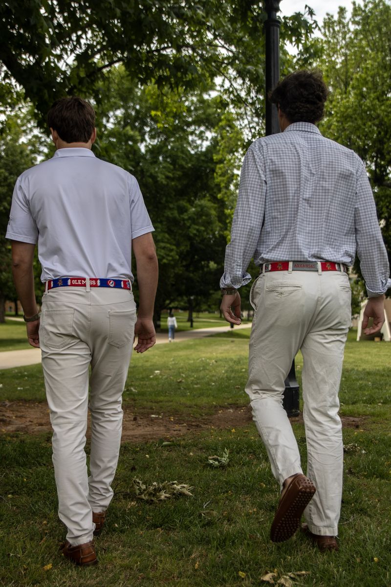 Two men in khakis and beaded belts walk across a lawn